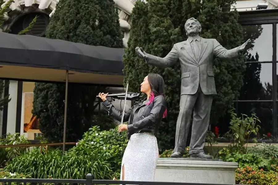 在费尔蒙特酒店，一名女子在托尼·班尼特雕像前演奏小提琴。.